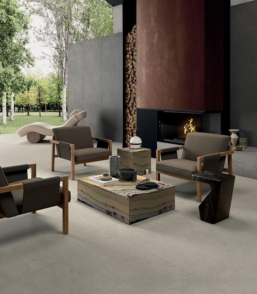 Contemporary living area with fireplace and garden view, featuring flooring from the Intense collection in Perle stone effect and wall covering from the Pigmenti collection in the Basalt shade.