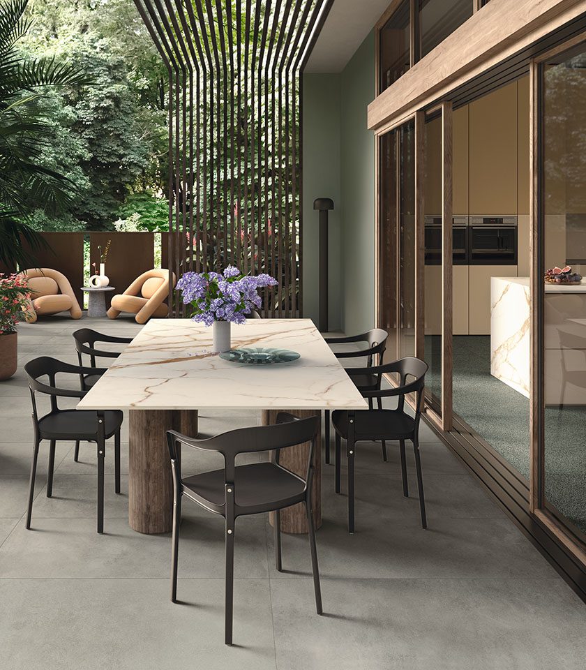 Contemporary outdoor dining area with flooring from the Masterpiece collection in Master Gray stone effect, Piece Alpi elements and a table featuring a surface from the Delight collection in Calacatta Oro marble effect.