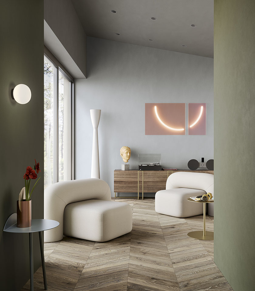 Contemporary living room with herringbone wood-effect flooring, sage green walls, white armchairs and design details.