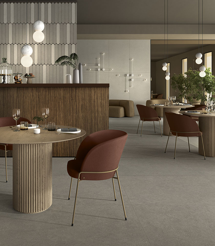 Contemporary restaurant with grey stone-effect flooring, sculptural tables, burgundy seating and wooden details.