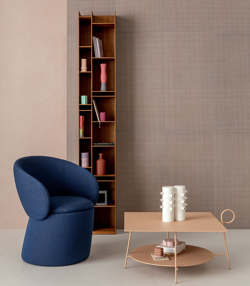 Contemporary interior with a blue armchair, blush-toned coffee table, wooden shelving unit and micro-patterned feature wall.