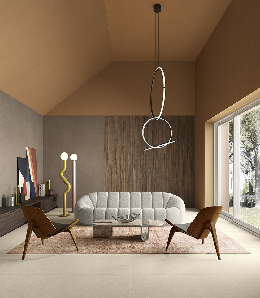 Contemporary living room with beige stone-effect flooring, a sculptural sofa, wooden armchairs and large windows overlooking the greenery.
