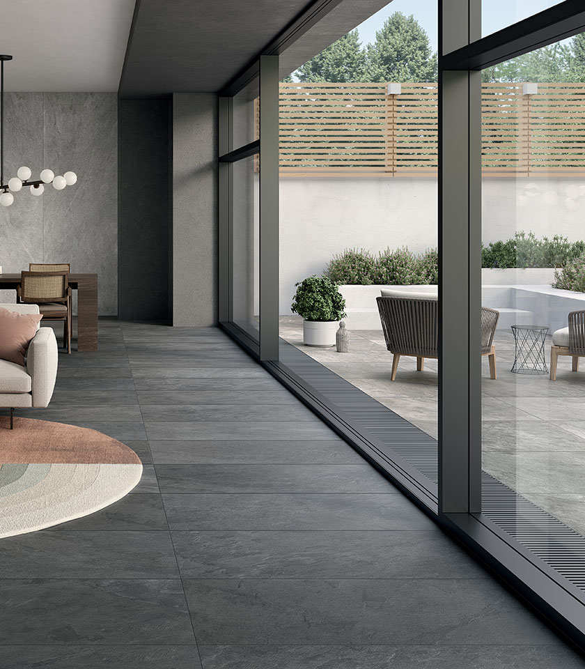 Contemporary space with grey stone-effect flooring extending seamlessly from indoors to outdoors, large glass windows and a terrace furnished with essential design.