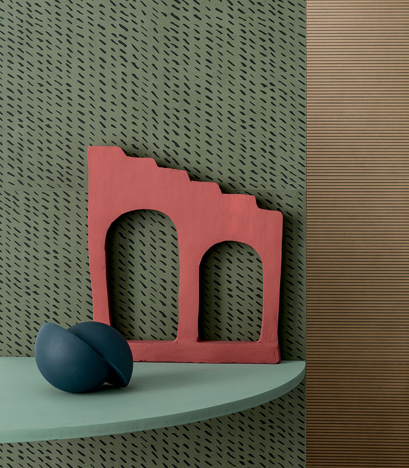 Decorative detail with green graphic-pattern wall covering, a red sculptural element and a shelf in natural tones.