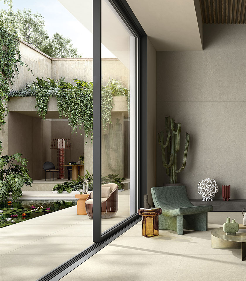 Indoor-outdoor space with light porcelain stoneware flooring, large glass doors, lush greenery and contemporary furnishings.
